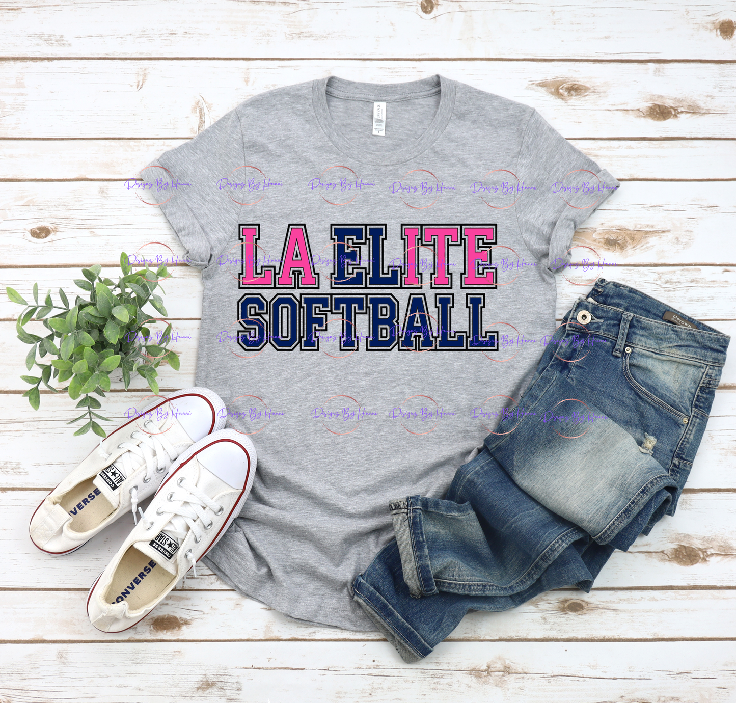 Gray t-shirt with 'LA ELITE SOFTBALL' text, white sneakers, and jeans on a wooden surface.